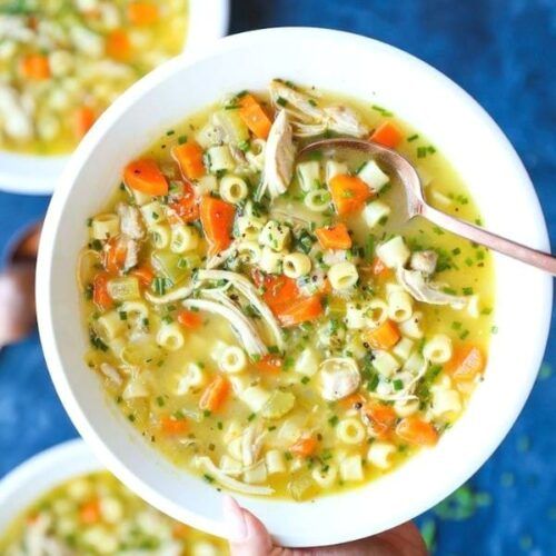 two bowls of chicken noodle soup on a blue surface