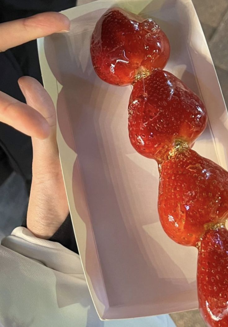 strawberries are arranged in the shape of hearts on a white platter, being held by someone's hand