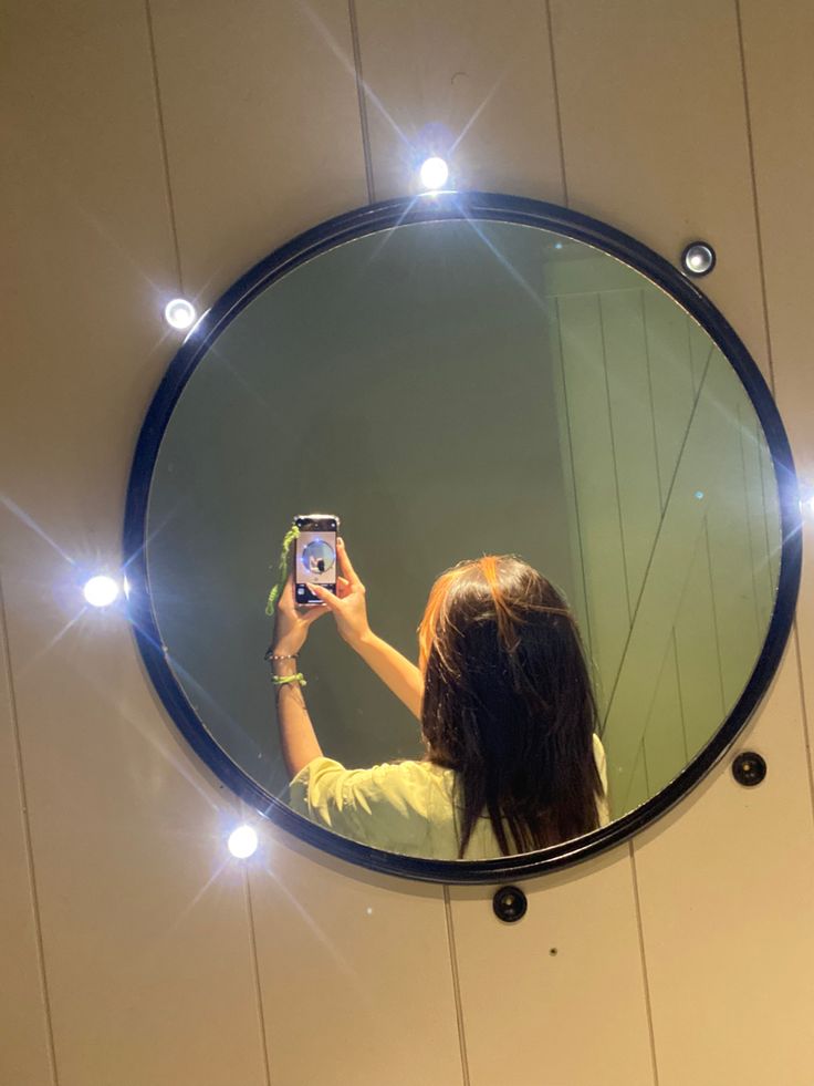 a woman taking a selfie with her cell phone in front of a round mirror