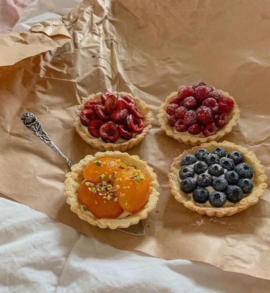 four pies with berries, oranges and blueberries in them on a piece of wax paper