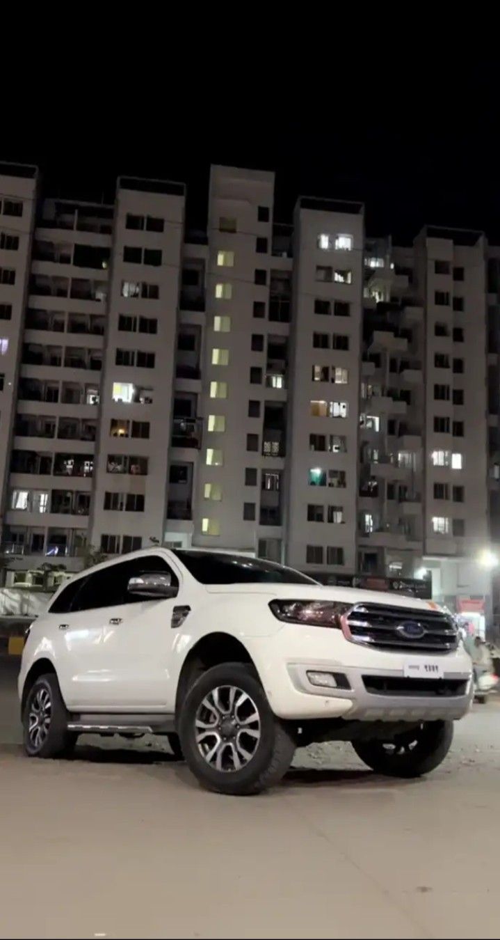 a white suv is parked in front of some tall buildings at night with its lights on