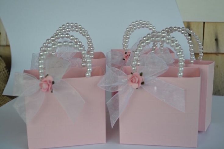 two pink gift bags with bows and pearls on them are sitting next to each other