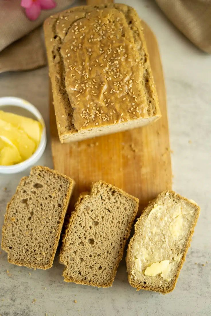 slices of bread sitting on top of a wooden cutting board next to butter and mustard