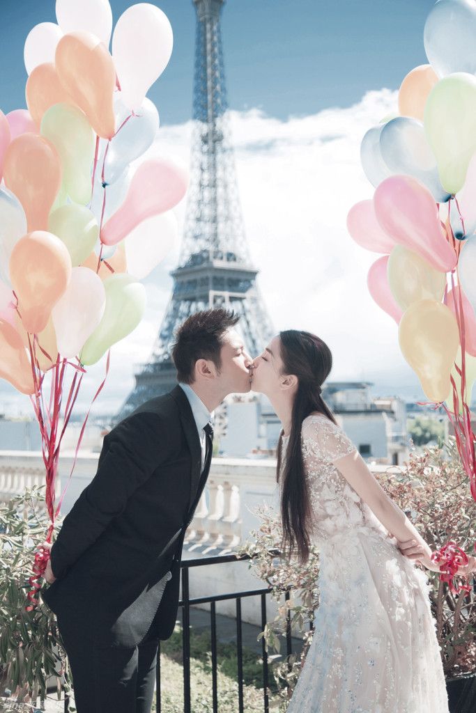 a man and woman kissing in front of the eiffel tower with balloons flying around them