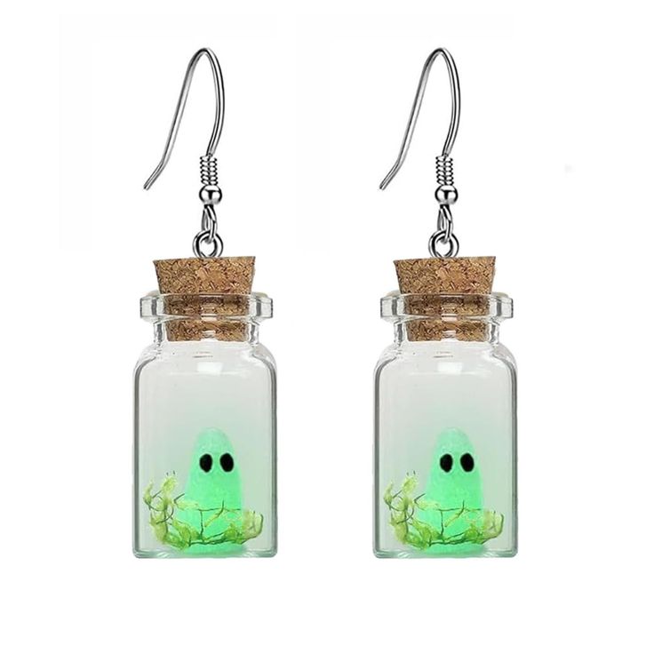 a pair of earrings with a green face in a glass jar