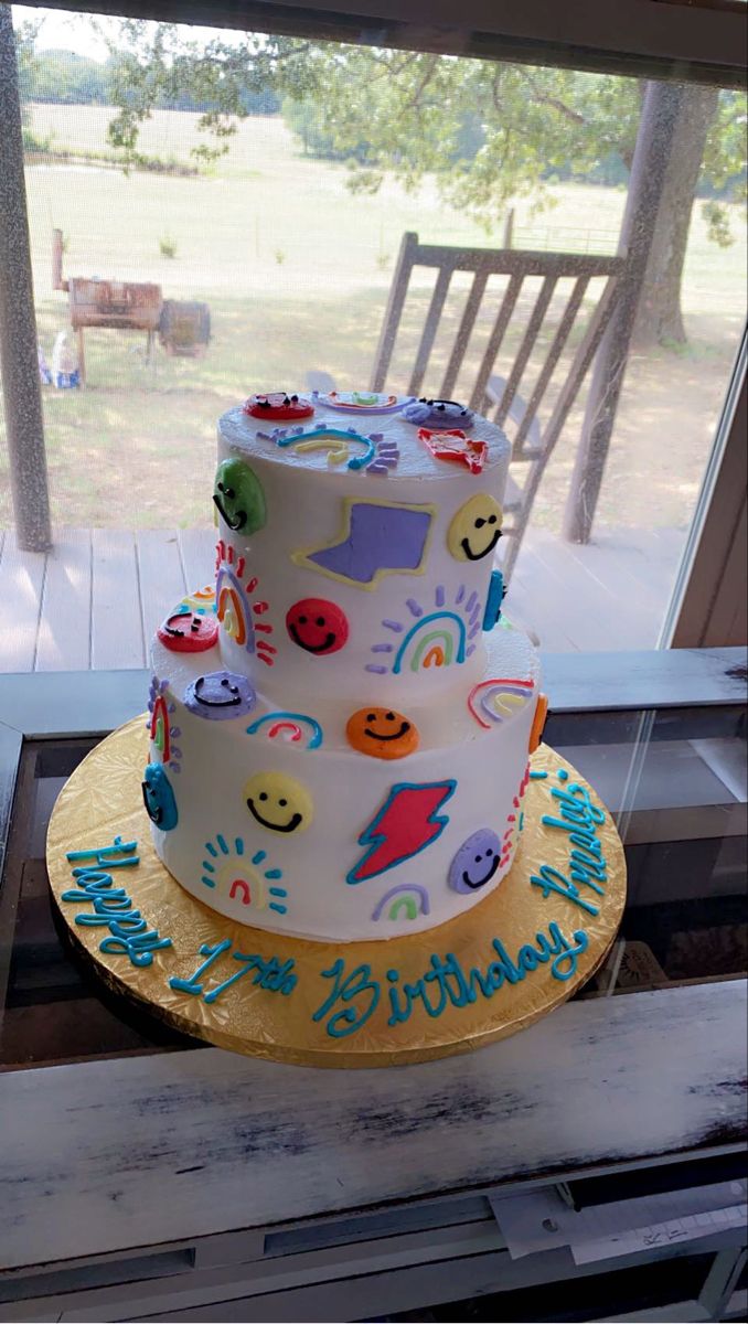 a three tiered birthday cake sitting on top of a table next to a window