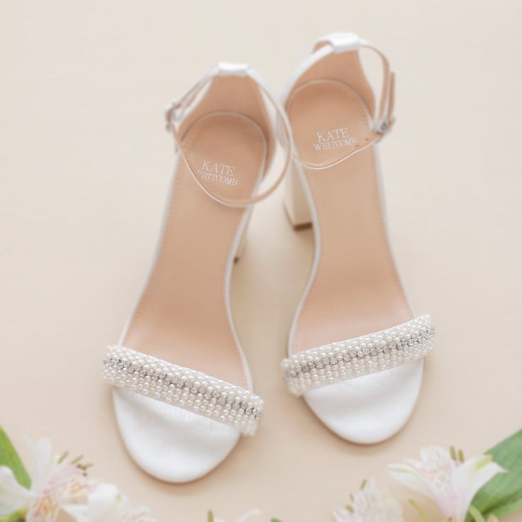 a pair of white shoes with pearls on the toes and heels are sitting next to flowers