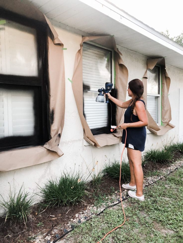 a woman using a power drill to paint the side of a house's window