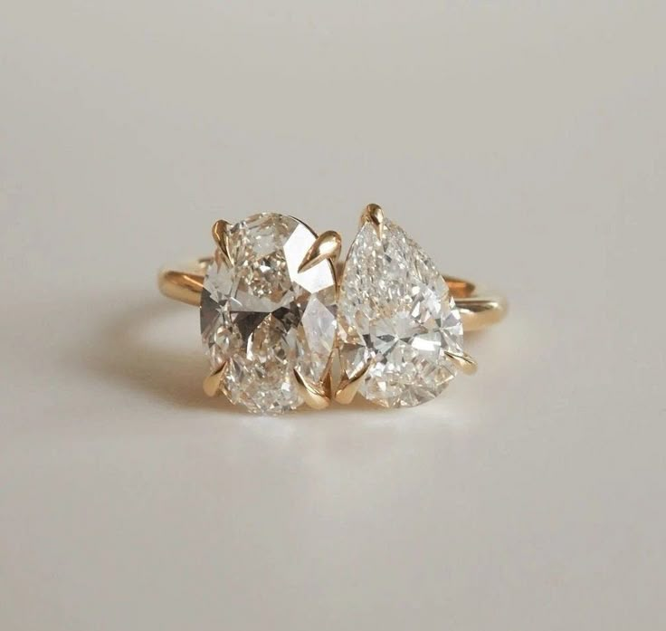 three pear shaped diamond engagement rings on a white surface with the top one in yellow gold