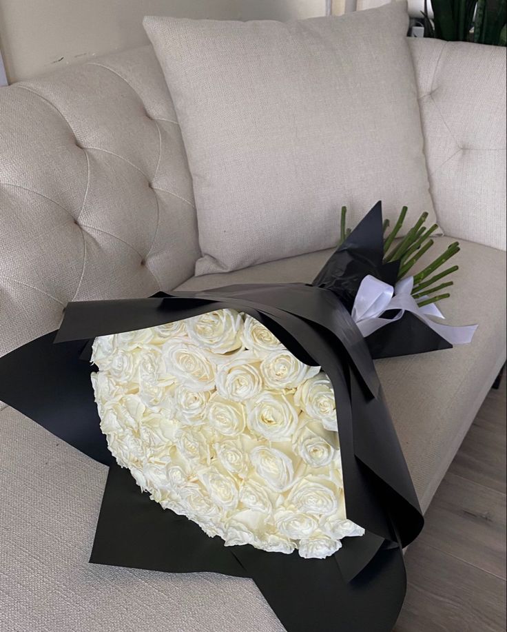 a bouquet of white roses wrapped in black paper on a couch with a pillow behind it