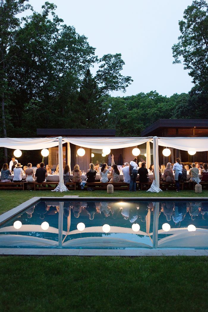 a group of people sitting at tables next to a swimming pool with lights on it