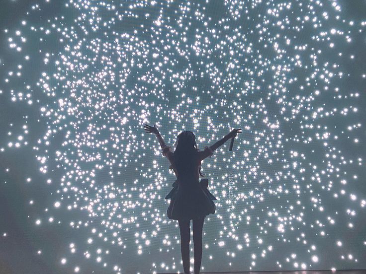 a woman standing on top of a stage with her arms outstretched in front of fireworks