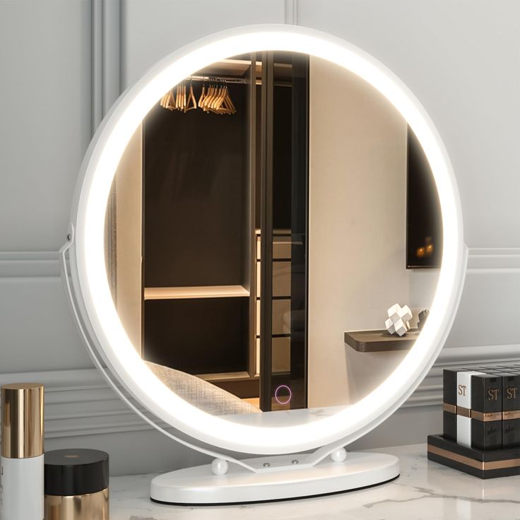 a round mirror sitting on top of a table next to a book shelf and vase