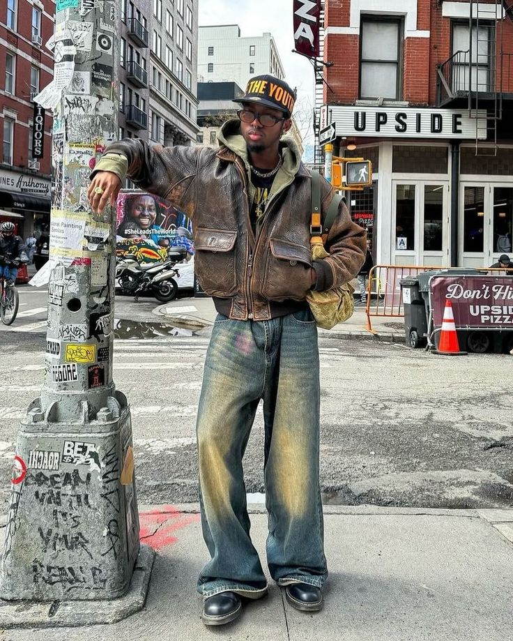 Vintage Vibe 🍩 How about his color? 📸 @knawtkai 🇺🇸 🧢Cap : free the youth 👔Hoodie : trendtvision 👞Shoes : dr.martens 👜Bag : louis vuitton Embodying the vintage vibes of American streets, this man’s outfit exudes timeless coolness. The combination of the vintage brown leather jacket and washed baggy jeans sets the tone, while the ‘Trendtvision’ khaki zipped hoodie and black printed shirt add depth to the ensemble. Elevating the look further, the ‘Dr. Martens’ black boots and ‘Free the Y... Brown Docs Outfit Men, Fits With Docs, Vintage Jacket Outfit Men, Men’s Leather Jackets Outfit, Brown Jacket Men Outfit, Cool Leather Jackets, Vintage Baggy Outfit, Baggy Jeans With Boots, Leather Shoes Men Outfit