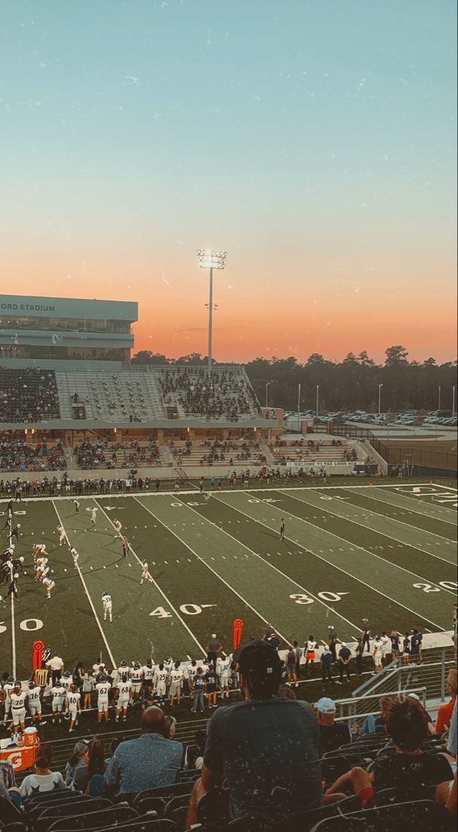 an empty football stadium filled with people watching the sun go down in the distance,