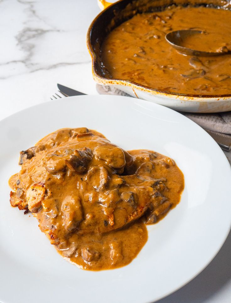 a white plate topped with meat covered in gravy next to a casserole dish