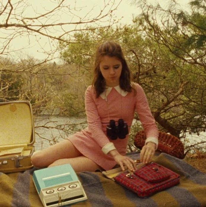 a woman sitting on a blanket with an open suitcase and other items in front of her