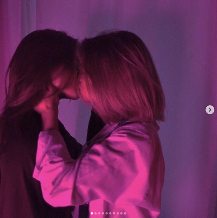 two women are kissing in front of a purple background