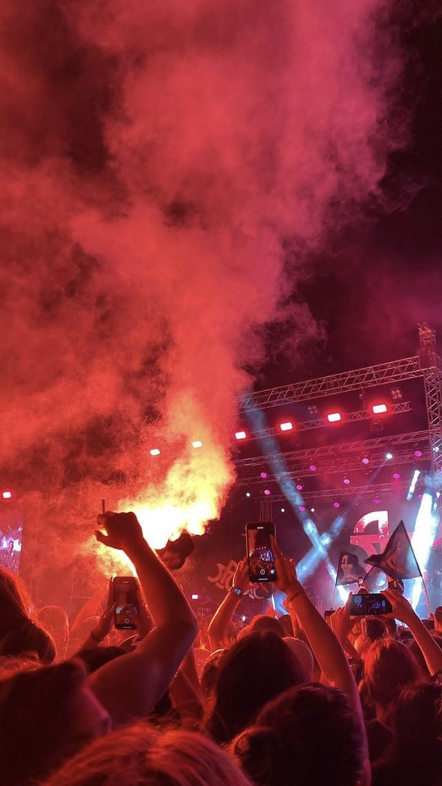 a crowd at a concert with their hands up in the air and fireworks coming from behind them