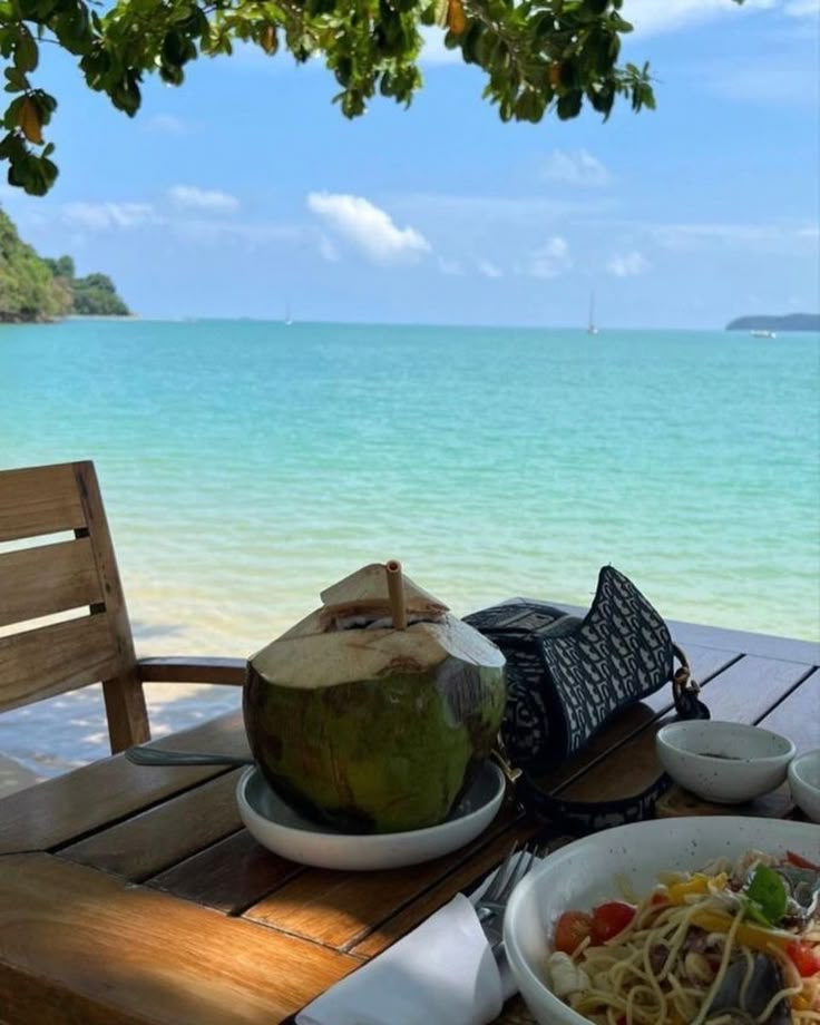 there is a bowl of food on the table by the ocean with a coconut in it