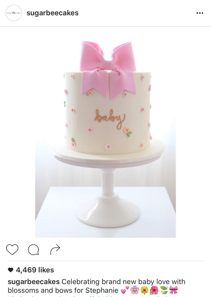 a white cake with pink bows and the words baby on it is sitting on a pedestal