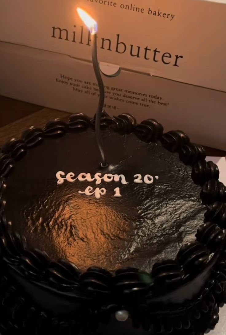 a chocolate cake with a single lit candle on it and a box in the background