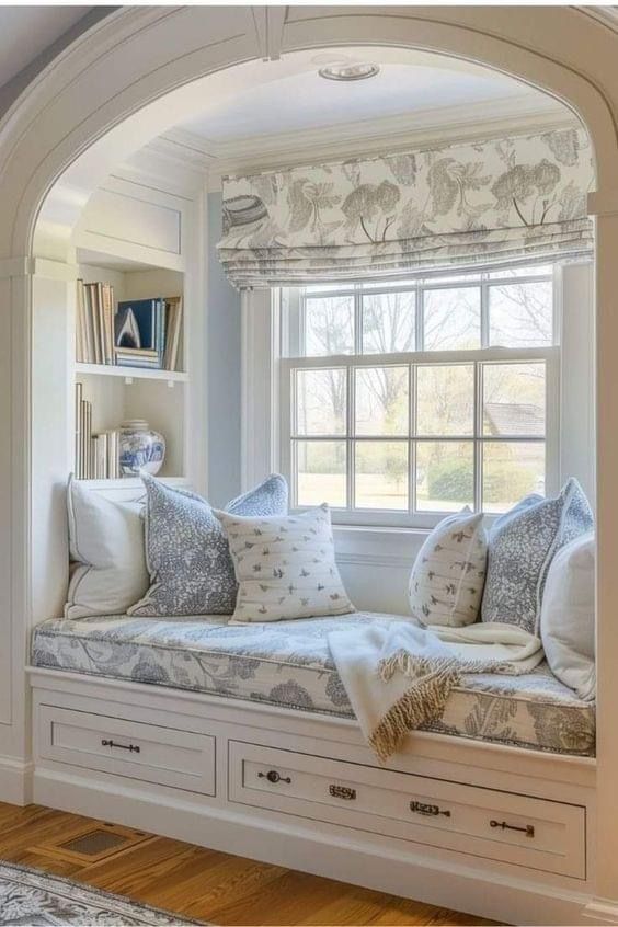 a window seat with pillows on it in front of a book shelf and bookshelf