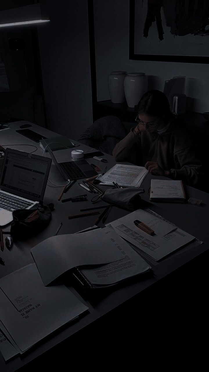 a person sitting at a desk in the dark with their laptop and papers on it