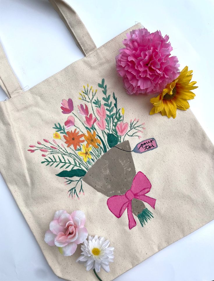 a tote bag with flowers painted on it and a pink flower in the center