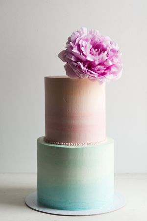 a three tiered cake with pink and blue frosting on top, topped with a single flower