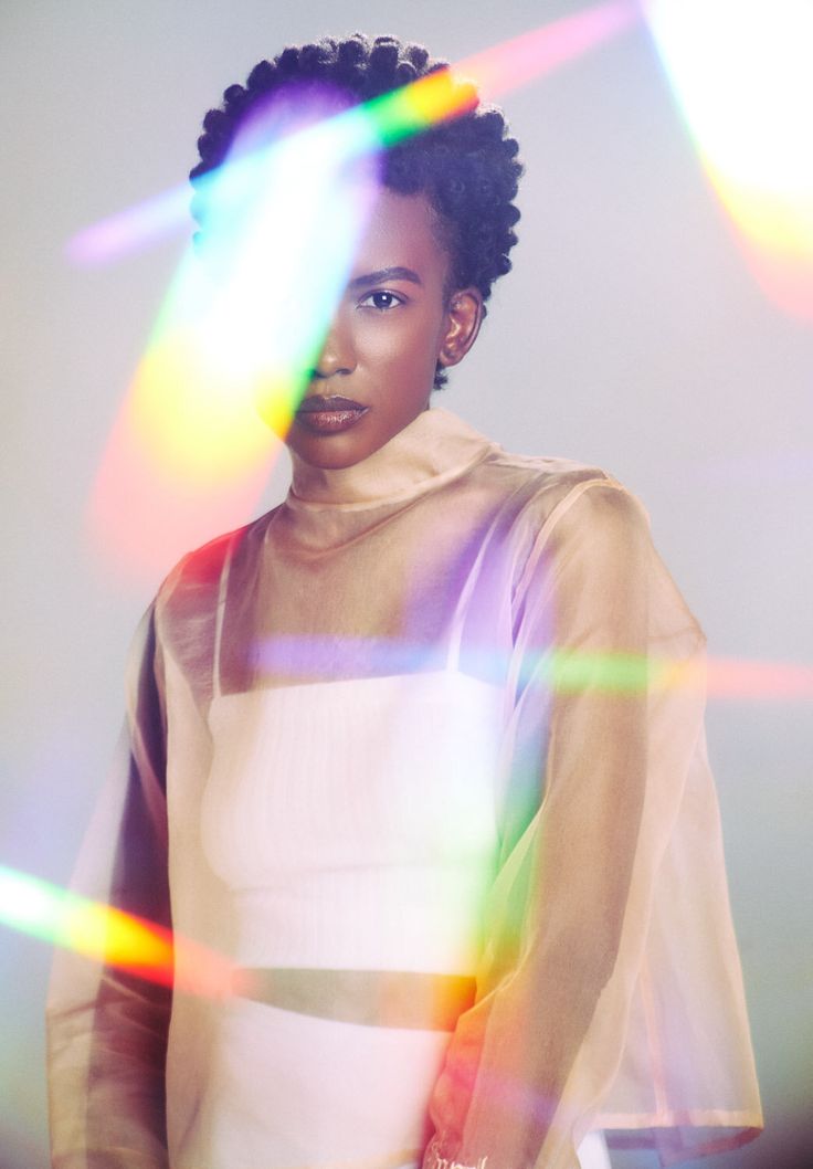 a woman with an afro standing in front of bright colored lights and looking at the camera