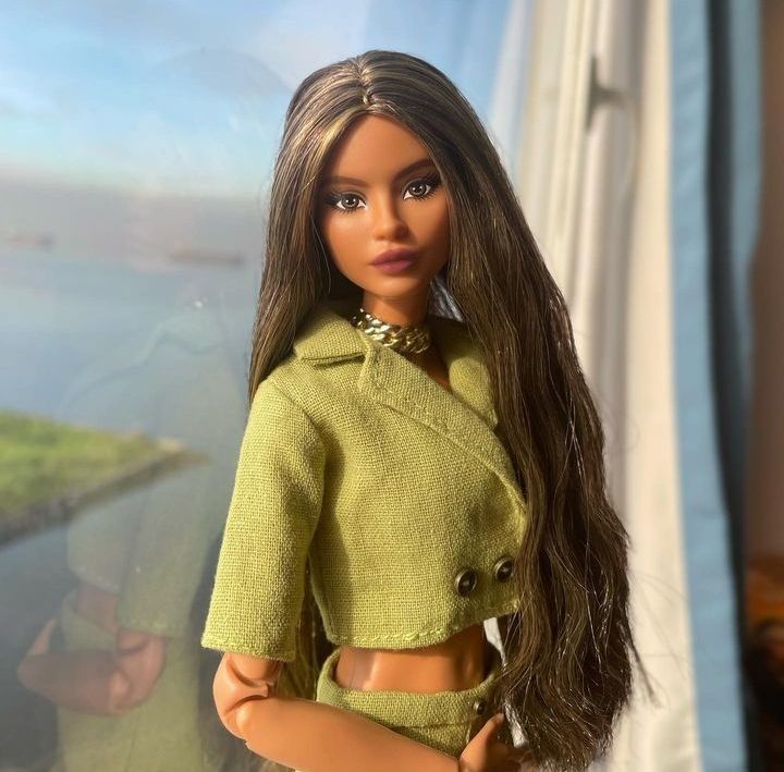 a doll with long hair is posed in front of a window, wearing a green outfit