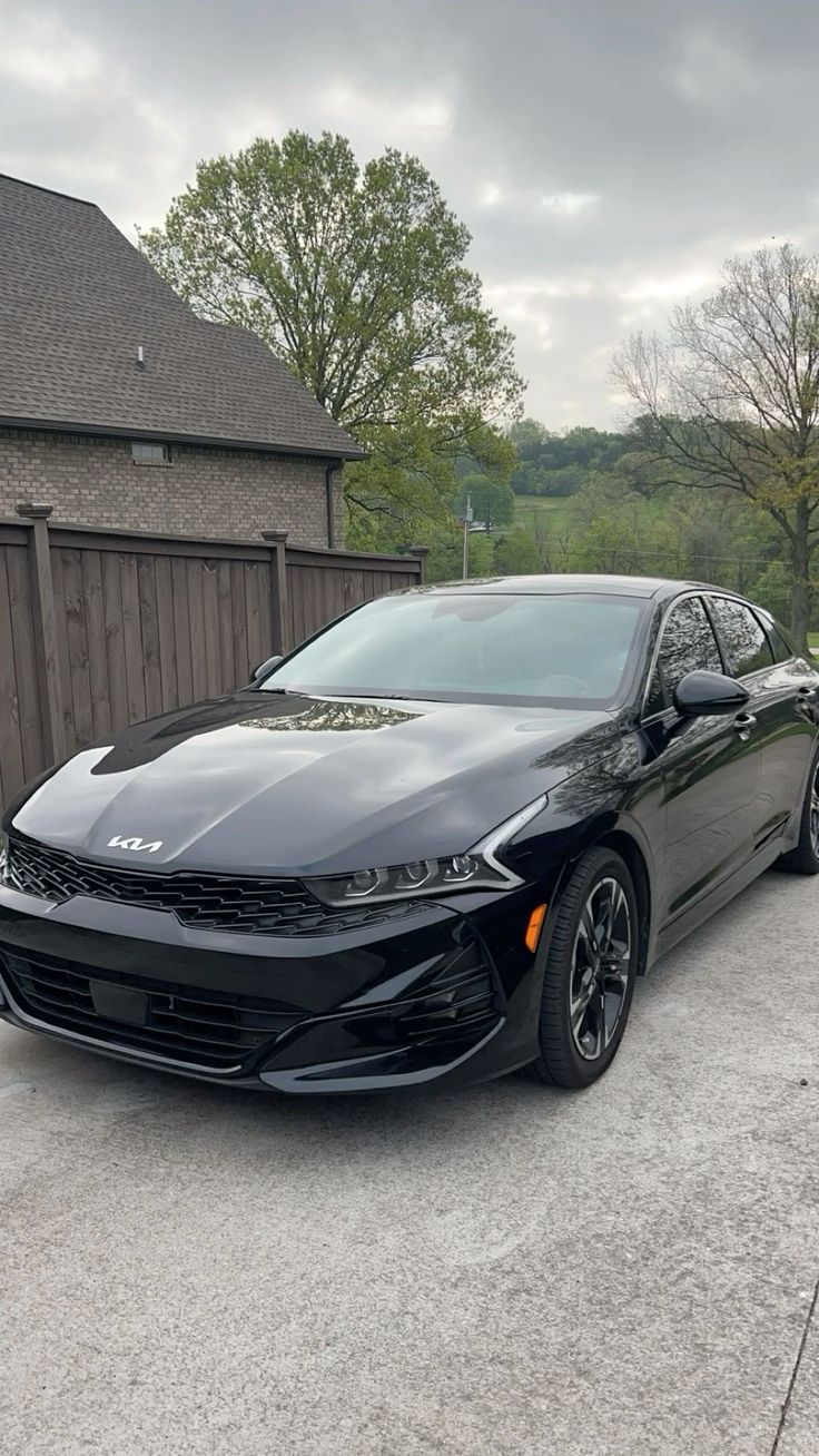 a black sports car parked in front of a house on a driveway next to a wooden fence