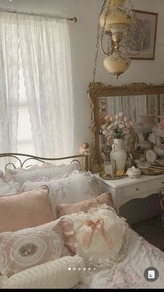 a white bed sitting in a bedroom next to a window covered in pink and gold pillows