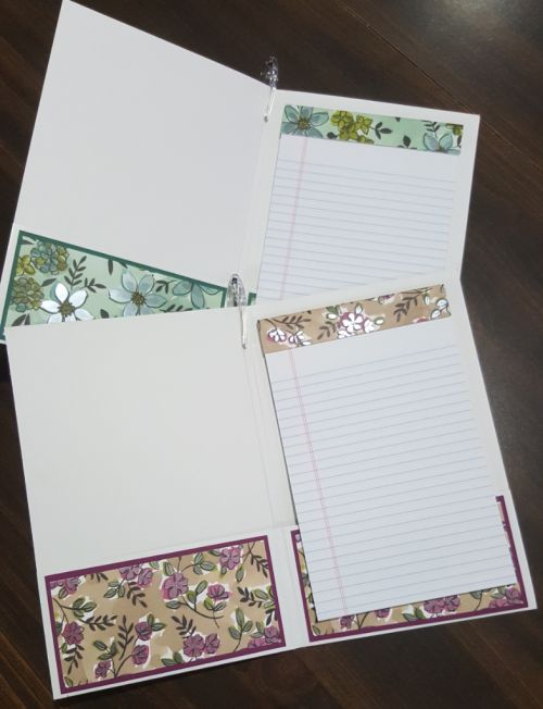 three open notebooks sitting on top of a wooden table covered in papers and lined with floral designs