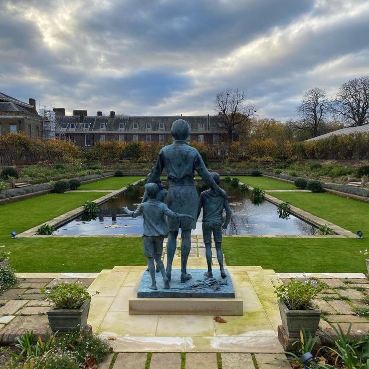 a statue of a man and two dogs in a formal garden setting with green grass