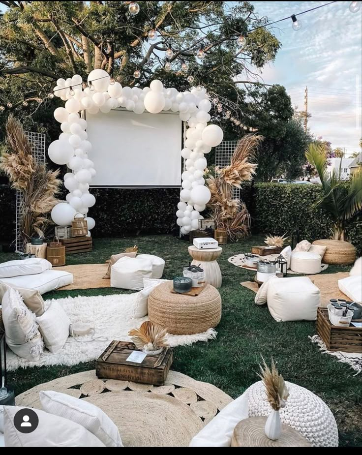 an outdoor movie party with white balloons and pillows on the grass in front of a large screen