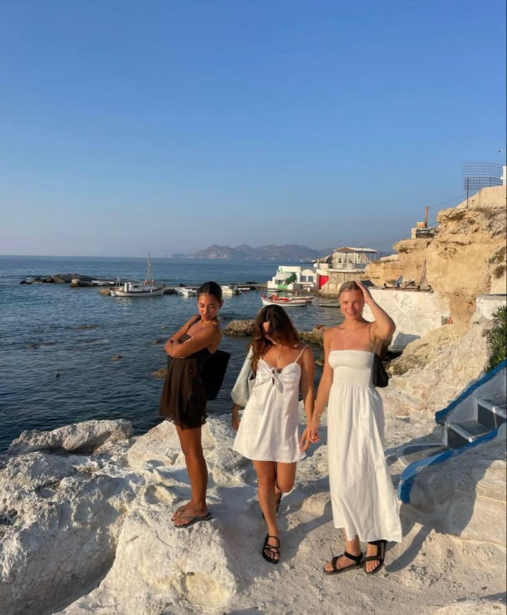 three women in white dresses standing on rocks by the water