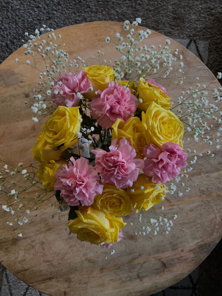 a bouquet of yellow and pink flowers sitting on top of a wooden table with baby's breath