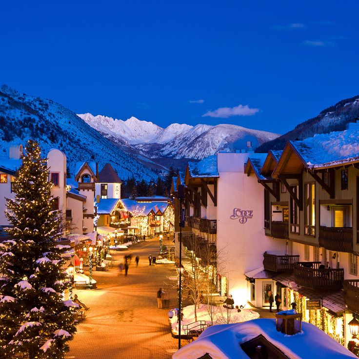 the town is lit up for christmas and it's surrounded by snow covered mountains