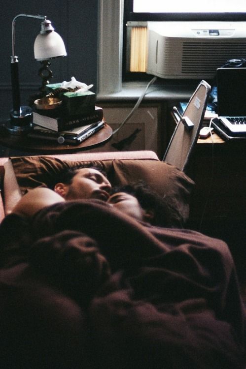 a woman laying in bed with her head on the pillow and looking at a laptop