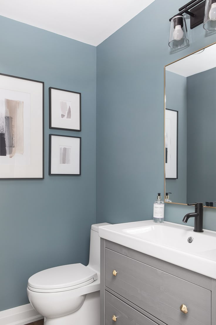 a white toilet sitting under a bathroom mirror next to a sink in a room with blue walls