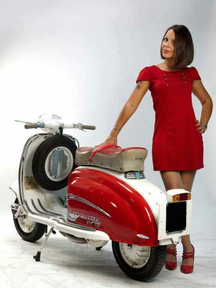 a woman in a red dress is standing next to a motor scooter and posing for the camera