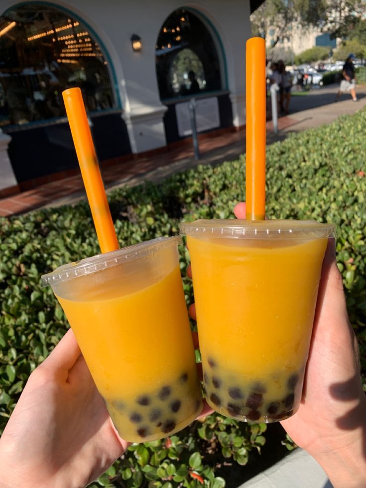 two people holding up glasses with orange juice and chocolate chips on them in front of bushes