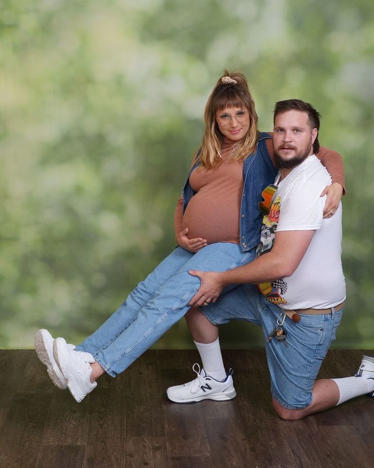 a man and woman pose for a photo in front of a green background with trees