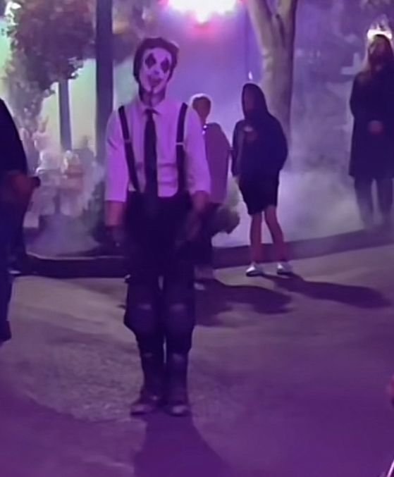 a man wearing a skeleton mask and suspenders walks down the street with other people