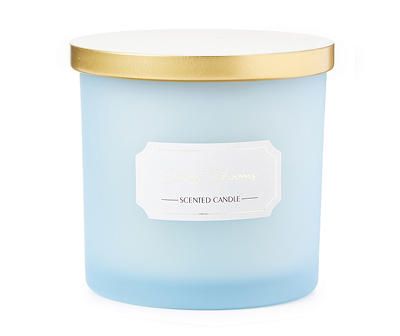 a blue candle with a gold lid sitting on a white surface, it has a label that reads scented candle