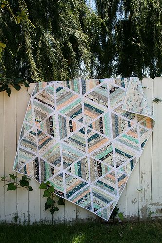 a patchwork quilt hanging on the side of a white fence with trees in the background