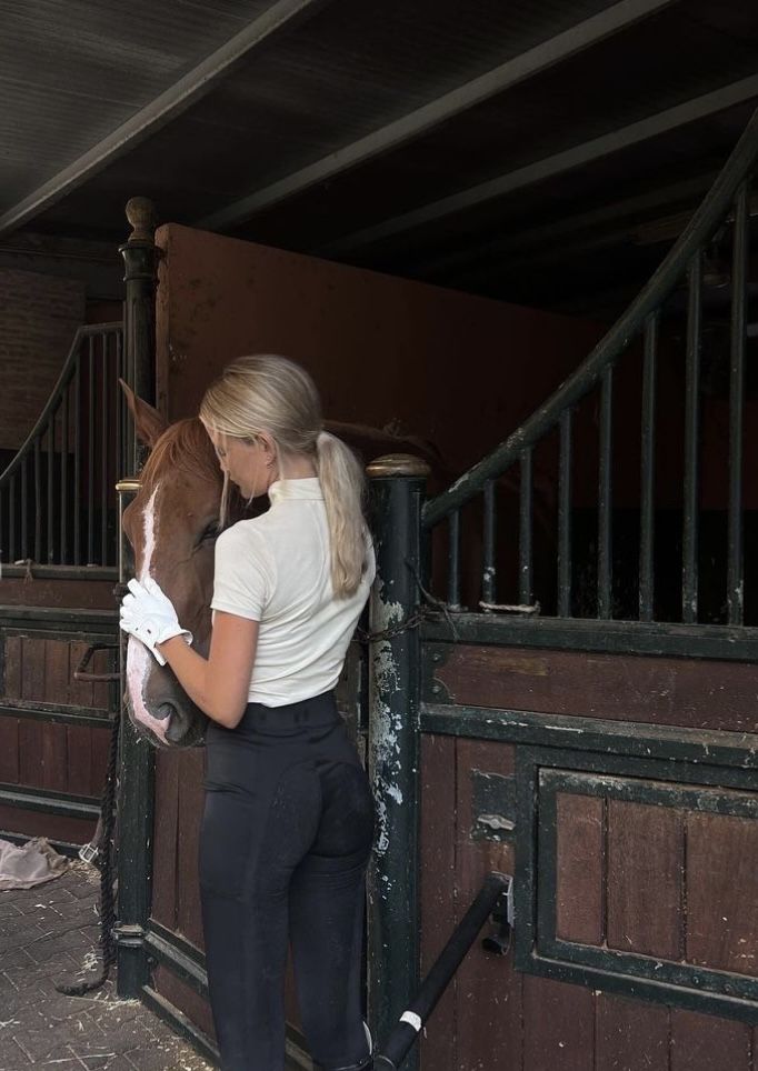 a woman standing next to a brown and white horse in a stable with its head on the gate