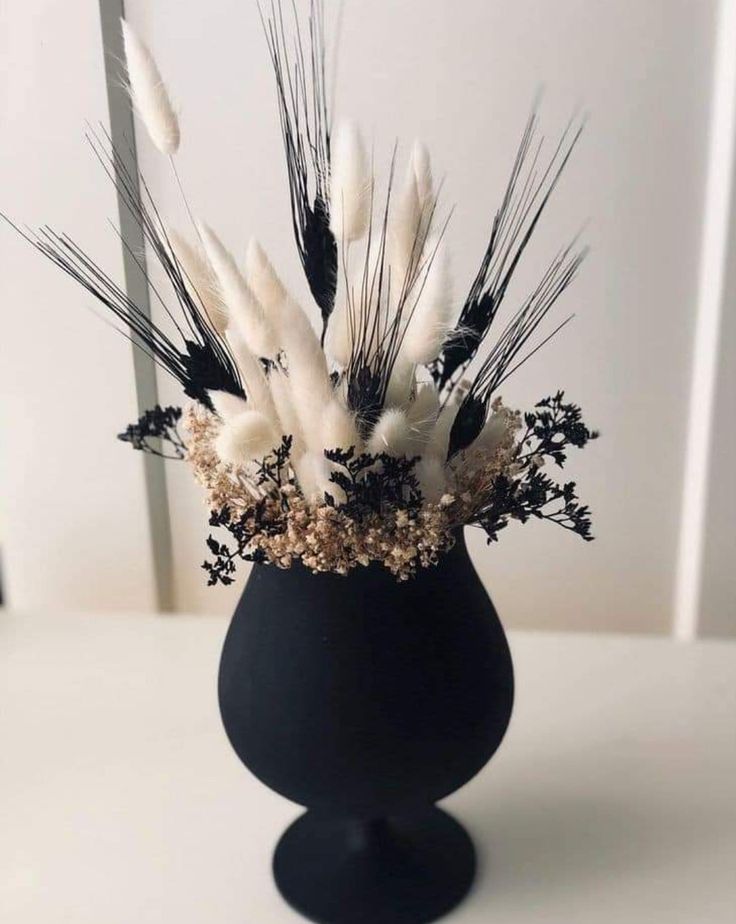 a black vase filled with white flowers and feathers